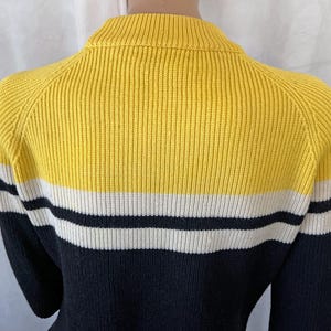 Puede incluir: Un su&eacute;ter a rayas amarillas, blancas y negras. El su&eacute;ter tiene una textura acanalada y un cuello alto. Las mangas son negras. El su&eacute;ter est&aacute; hecho de un material suave y c&oacute;modo.