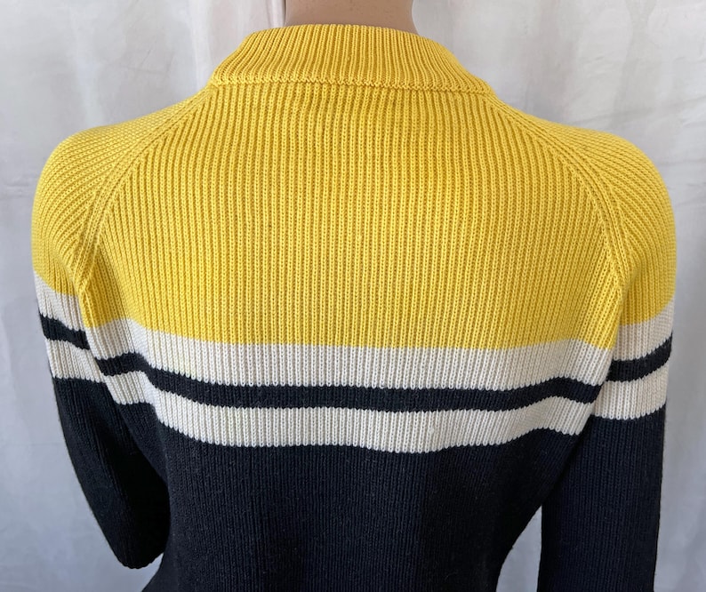 Puede incluir: Un su&eacute;ter a rayas amarillas, blancas y negras. El su&eacute;ter tiene una textura acanalada y un cuello alto. Las mangas son negras. El su&eacute;ter est&aacute; hecho de un material suave y c&oacute;modo.