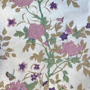 Könnte beinhalten: Stoff mit floralem Muster mit großen rosa Blüten, lila Akzenten und grünen Blättern auf cremefarbenem Hintergrund. Das Design umfasst Schmetterlinge und ein strukturiertes Aussehen, wodurch eine Vintage-Ästhetik entsteht. Geeignet für verschiedene Bastelprojekte.
