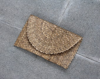 Könnte beinhalten: Eine braune geflochtene Clutch mit einem einzigartigen, strukturierten Design. Die Clutch ist aus natürlichen Materialien gefertigt und hat eine leicht abgerundete Form.
