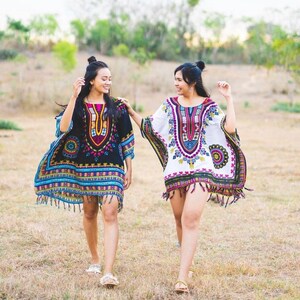 Puede incluir: Dos personas con kaftanes de patrones coloridos con flecos recorren un campo de hierba. Los kaftans tienen dise&ntilde;os geom&eacute;tricos y florales.