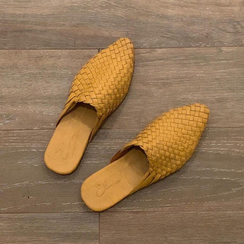 May include: A pair of woven leather yellow mules with pointed toes. The shoes have a simple design and are made of a soft, comfortable material.
