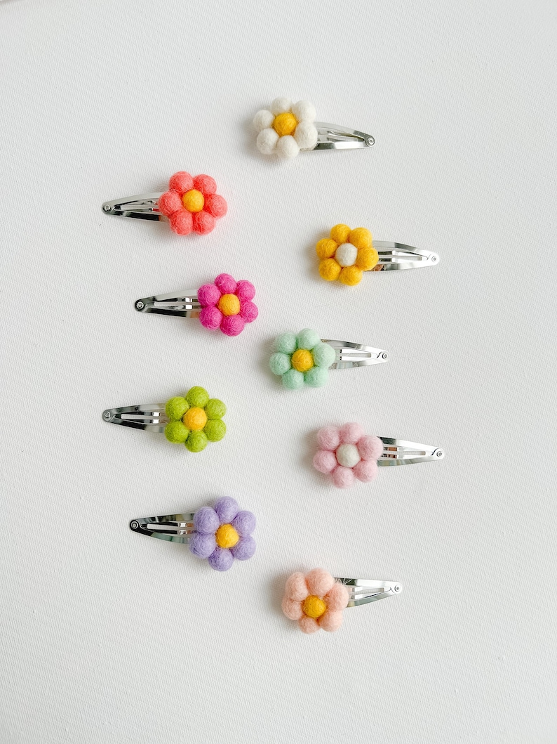 K&ouml;nnte beinhalten: Satz mit zehn bunten Filzblumen-Haarklammern. Jede Klammer zeigt eine Blume in einer anderen Farbe mit einer gelben Mitte. Die Klammern sind perfekt, um jeder Frisur einen Hauch von Verspieltheit zu verleihen.