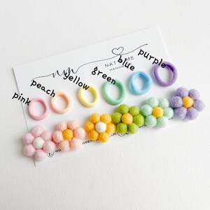 K&ouml;nnte beinhalten: Ein Set aus bunten Haargummis mit passenden Filzblumen-Haarklammern. Die Haargummis sind in den Farben Pink, Pfirsich, Gelb, Gr&uuml;n, Blau und Lila. Die Blumen haben die gleichen Farben wie die Haargummis.