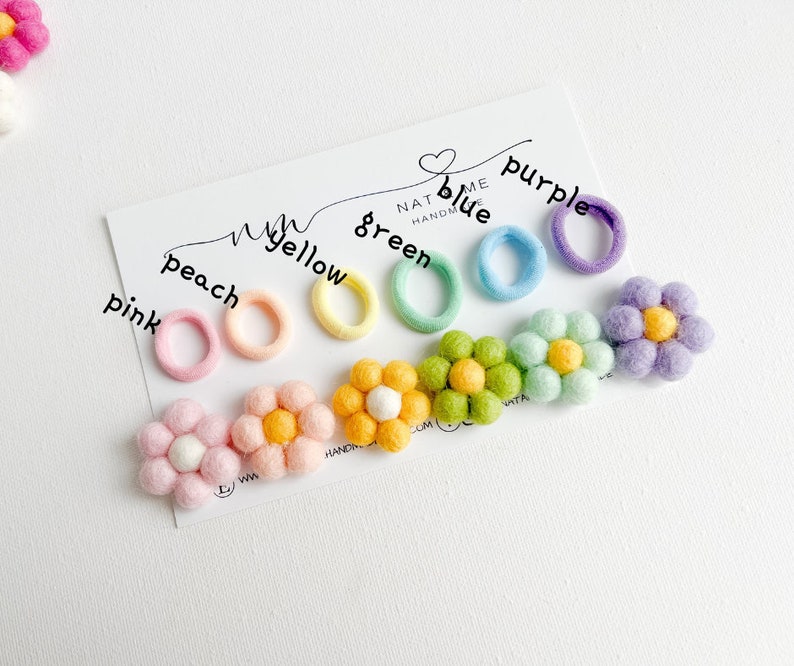 K&ouml;nnte beinhalten: Ein Set aus bunten Haargummis mit passenden Filzblumen-Haarklammern. Die Haargummis sind in den Farben Pink, Pfirsich, Gelb, Gr&uuml;n, Blau und Lila. Die Blumen haben die gleichen Farben wie die Haargummis.