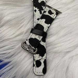 Op de afbeelding: Zwart-witte Apple Watch band met koeienprint. De band is gemaakt van leer en heeft een metalen gesp.