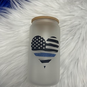 Peut inclure: Un bocal en verre givré avec un couvercle en bois, présentant un motif en forme de cœur avec un drapeau américain et un ruban bleu de police.