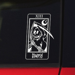 May include: A white vinyl sticker of the Death tarot card. The card features a black and white illustration of the Grim Reaper holding a scythe. The card number, XIII, is at the top of the card. The word "DEATH" is written in a gothic font at the bottom of the card.