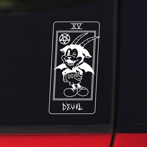 May include: A black and white sticker of a cartoon devil with horns and wings. The sticker is in the shape of a tarot card with the number XV and the word "DEVIL" written below the image.