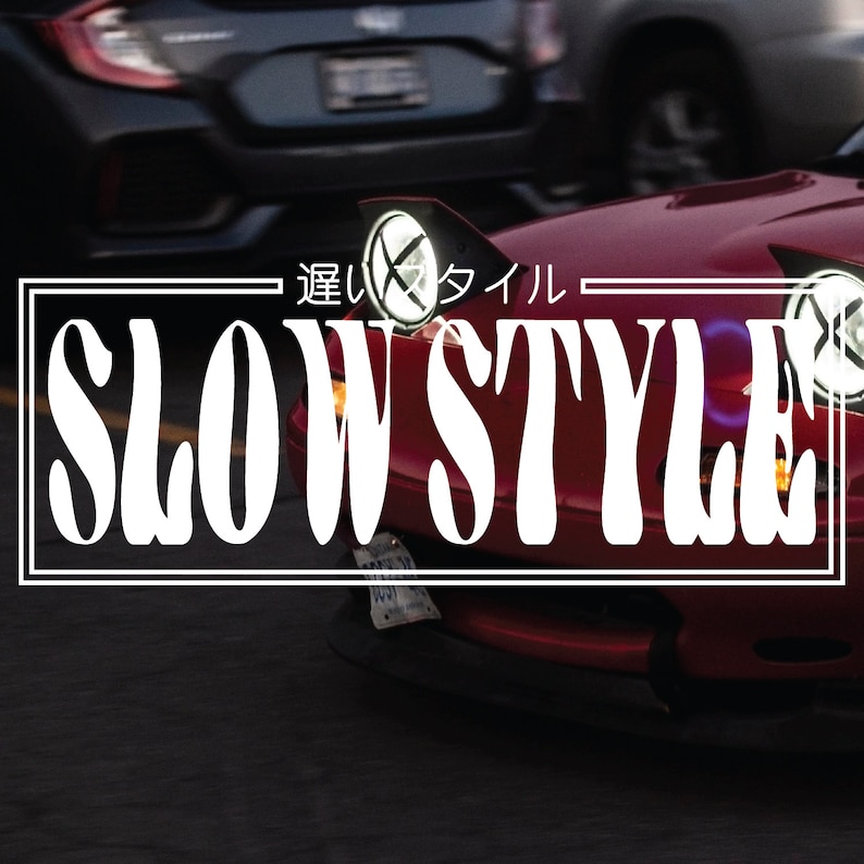 以下が含まれることがあります： 黒い背景に白い文字で「Slow Style」と書かれた赤い車。車は黒いバンパーと黒いグリルが付いている。車はピントが合っていて、背景はぼやけている。