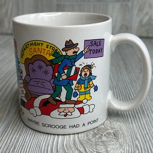 May include: White ceramic mug with a cartoon illustration of Santa Claus, a man in a blue coat, and a child in a red coat. The illustration depicts a scene from the department store during the Christmas season. The text on the mug reads "Department Store Santa" and "Maybe Scrooge had a point".