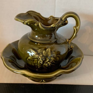 May include: A green ceramic pitcher with a grape design and a matching bowl. The pitcher has a handle and a wide mouth.