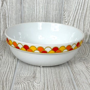 May include: White ceramic bowl with a colorful geometric pattern around the rim. The pattern features red, orange, and yellow circles on a white background.