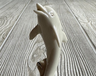 May include: A white porcelain dolphin figurine with gold accents, leaping out of the water. The dolphin is positioned on a wave-like base.