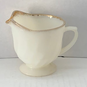 May include: A small white creamer with a gold rim and a footed base.