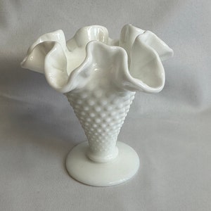 May include: A white milk glass bud vase with a ruffled top and a textured, dimpled base.