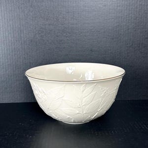 May include: A white ceramic bowl with a gold rim and a raised leaf design.