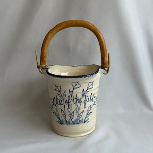 May include: A white ceramic pitcher with a blue floral design and the text "Lilies of the field". The pitcher has a wooden handle.