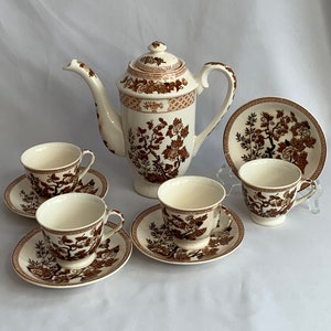 Puede incluir: Un juego de té marrón y blanco con un patrón floral. El juego incluye una tetera, cuatro tazas y cuatro platillos.