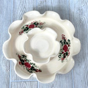 以下が含まれることがあります： クリーム色のスカラップエッジのサービング皿。3つのセクションがあり、赤と緑のアクセントのフローラルデザインが特徴です。セラミック製で、前菜や軽食の提供に適しています。