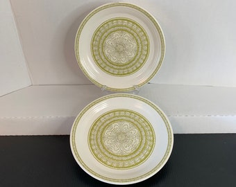May include: Two white ceramic dinner plates with a green and white floral design. The plates have a raised rim and a scalloped edge.