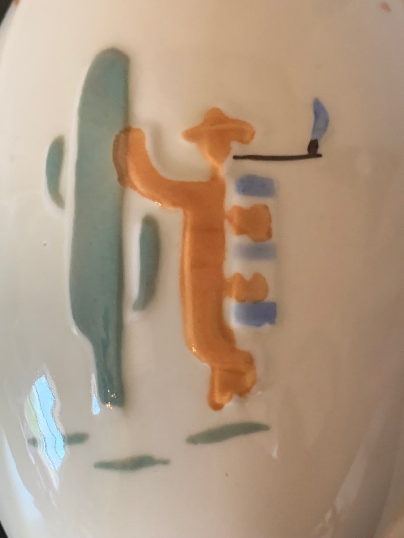 May include: A ceramic figurine of a person holding a stick with a flame on the end. The person is wearing a hat and has a blue and white striped shirt. The figurine is painted in shades of blue, green, and orange.
