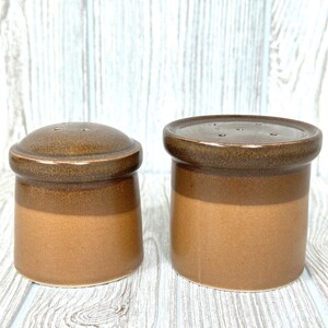 以下が含まれることがあります： 2つの茶色のセラミック製塩コショウ入れのセット。2色の釉薬がかかっています。塩コショウ入れは、塩とコショウを出すための穴のある丸いトップを持っています。
