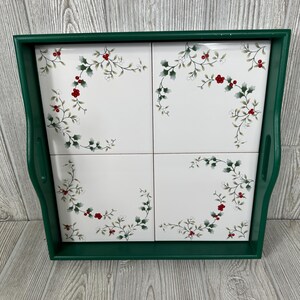 May include: A green wooden tray with four white ceramic tiles. Each tile features a green holly leaf and red berry design.