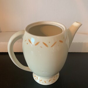 May include: A white ceramic teapot with a brown design. The teapot has a round body and a spout on the side. The teapot has a handle and a lid.