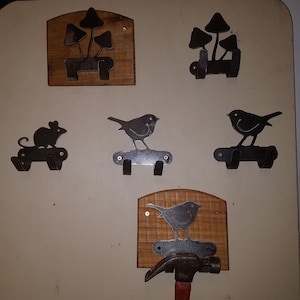 May include: A set of six metal wall hooks featuring various designs, including mushrooms, birds, and a mouse. The hooks are mounted on wooden plaques with a natural wood grain finish.