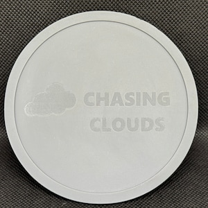 Puede incluir: Un posavasos redondo gris con el texto "CHASING CLOUDS" y un gráfico de nube.