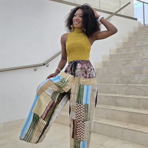 May include: Mustard yellow sleeveless top paired with patchwork wide-leg pants. The pants feature a variety of fabric patterns, including stripes and geometric designs, in shades of blue, gold, and burgundy. The outfit is worn in a bright, indoor setting.