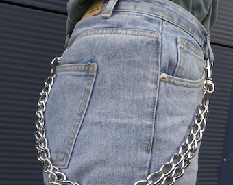 May include: Light blue denim jeans with a silver chain attached to the belt loops. The chain is made of thick, interlocking links and hangs down the side of the jeans. The jeans have a classic five-pocket design.
