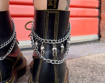 May include: Black leather boots with yellow stitching and a silver chain ankle bracelet with tooth charms. The ankle bracelet is layered with two chains.