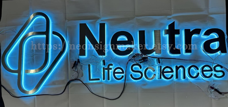 May include: A custom-made illuminated sign with the text "Neutra Life Sciences" in black letters with a blue halo. The sign is made of stainless steel and has a modern design.