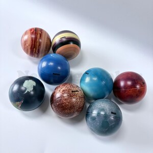 May include: A collection of nine spherical planet models, each with unique colors and surface patterns. The planets include Earth, Neptune, and Saturn, with their names printed on them. The sizes appear to be approximately 3 inches in diameter.
