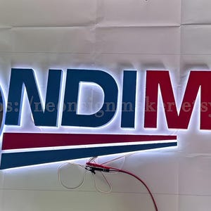 May include: A white illuminated sign with the text "ONDIMAX" in blue and red letters. A globe with a blue and grey map of the world is on the left side of the sign.