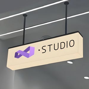 May include: A rectangular, illuminated sign suspended from the ceiling. The sign is cream-colored with black text that reads "STUDIO." A purple infinity symbol is on the left. The sign is hanging from two black rods.