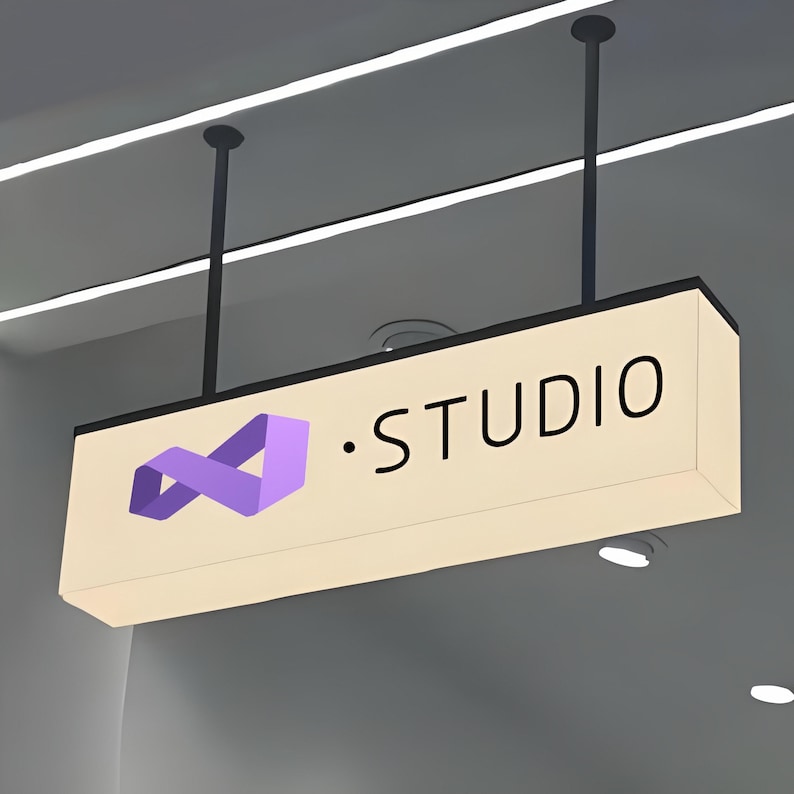 May include: A rectangular, illuminated sign suspended from the ceiling. The sign is cream-colored with black text that reads "STUDIO." A purple infinity symbol is on the left. The sign is hanging from two black rods.