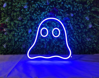May include: A blue neon ghost sign with a white outline and two circular eyes. The neon sign is displayed against a backdrop of green foliage and purple flowers. The sign is lit up and casting a blue glow.