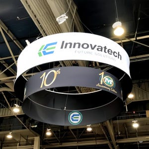 Puede incluir: Cartel colgante circular de dos niveles. El nivel superior es blanco con el logotipo de Innovatech y el texto "FUTURE SOLUTIONS". El nivel inferior es gris oscuro con "10th" en dorado y un logotipo de la "10th Anniversary Edition".