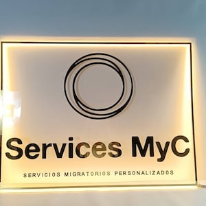 Puede incluir: Un letrero blanco iluminado con un logotipo circular negro y el texto "Services MyC" y "Servicios Migratorios Personalizados".