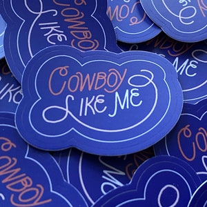 Pode incluir: Um monte de adesivos azuis e brancos com o texto "Cowboy Like Me" em uma fonte rosa e branca.