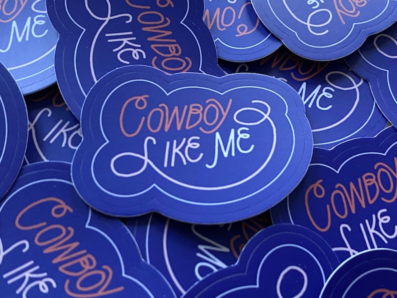 Pode incluir: Um monte de adesivos azuis e brancos com o texto "Cowboy Like Me" em uma fonte rosa e branca.