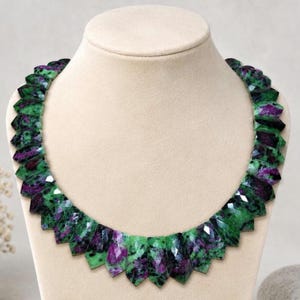 May include: A necklace composed of faceted, shield-shaped ruby in zoisite gemstones. Each stone features a distinct mottled pattern of vibrant green zoisite and deep magenta-purple ruby, arranged in a continuous, graduated collar-style design.