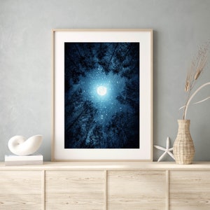 May include: A framed photograph of a full moon shining brightly in a dark blue night sky, surrounded by the silhouettes of trees. The moon is surrounded by a halo of light and the sky is filled with stars.