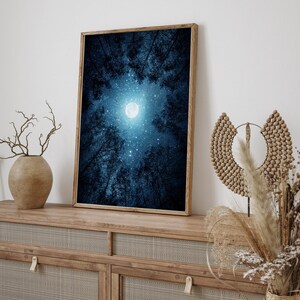 May include: A framed print of a night sky with a full moon and stars visible through the branches of trees. The sky is a deep blue color and the moon is white.