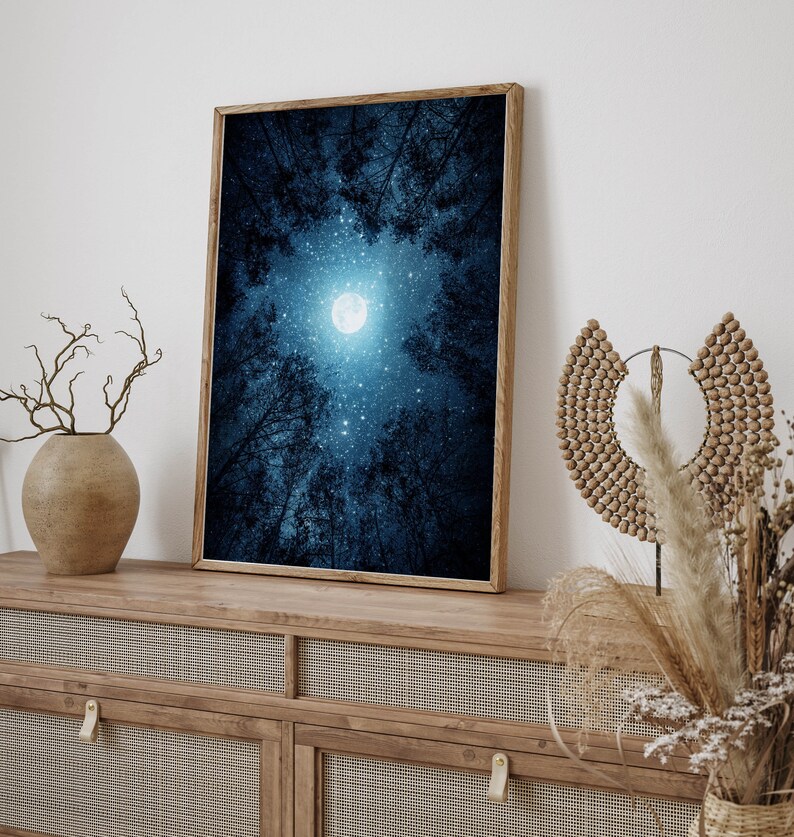 May include: A framed print of a night sky with a full moon and stars visible through the branches of trees. The sky is a deep blue color and the moon is white.