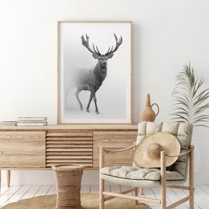 K&ouml;nnte beinhalten: Ein Schwarzwei&szlig;foto eines Hirsches mit gro&szlig;en Geweih, der auf einem nebligen Feld steht. Das Foto ist in einem hellen Holzrahmen gerahmt und h&auml;ngt an einer wei&szlig;en Wand &uuml;ber einem Holzschrank.