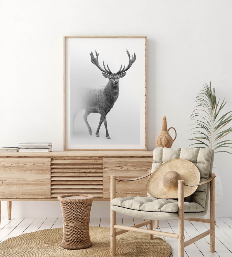 K&ouml;nnte beinhalten: Ein Schwarzwei&szlig;foto eines Hirsches mit gro&szlig;en Geweih, der auf einem nebligen Feld steht. Das Foto ist in einem hellen Holzrahmen gerahmt und h&auml;ngt an einer wei&szlig;en Wand &uuml;ber einem Holzschrank.